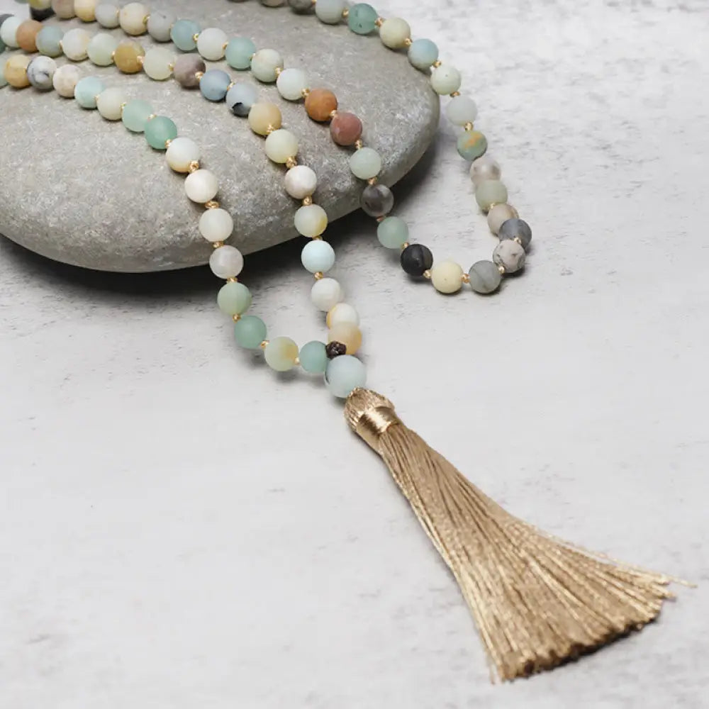 BWOOOH 108 Amazonite Beads Tassel Mala Bracelet on a natural wooden surface, showcasing its serene 6mm blue-green amazonite beads and an intricately woven tassel, reflecting spiritual balance and mindfulness.