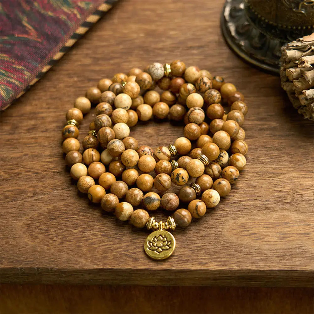 Close-up of BWOOOH 108-bead Picture Jasper Mala bracelet with earthy-toned, 8mm beads and a delicate round lotus-engraved charm, signifying courage and spiritual grounding for meditation.