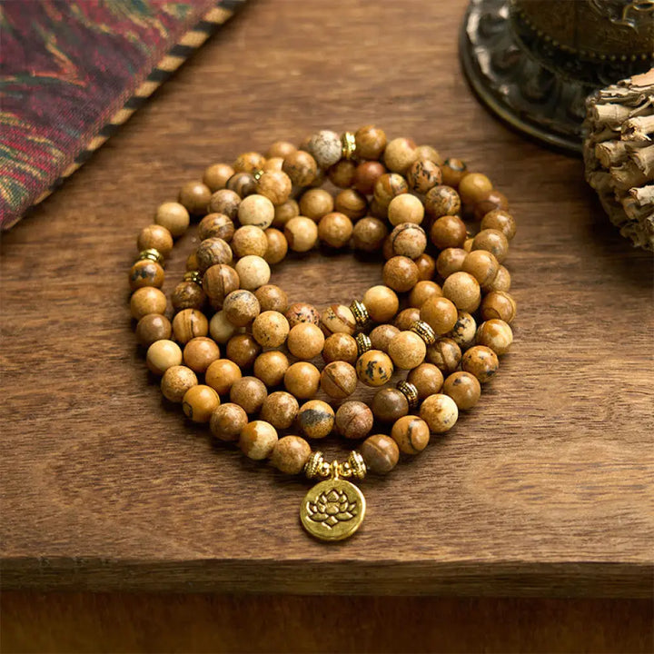 Close-up of BWOOOH 108-bead Picture Jasper Mala bracelet with earthy-toned, 8mm beads and a delicate round lotus-engraved charm, signifying courage and spiritual grounding for meditation.