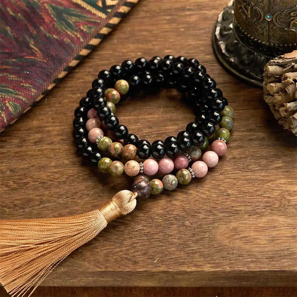 BWOOOH 108 Mala Beads crafted from Black Jasper and Rhodonite with a khaki tassel, resting on a meditation cushion, symbolizing grounding and emotional healing.