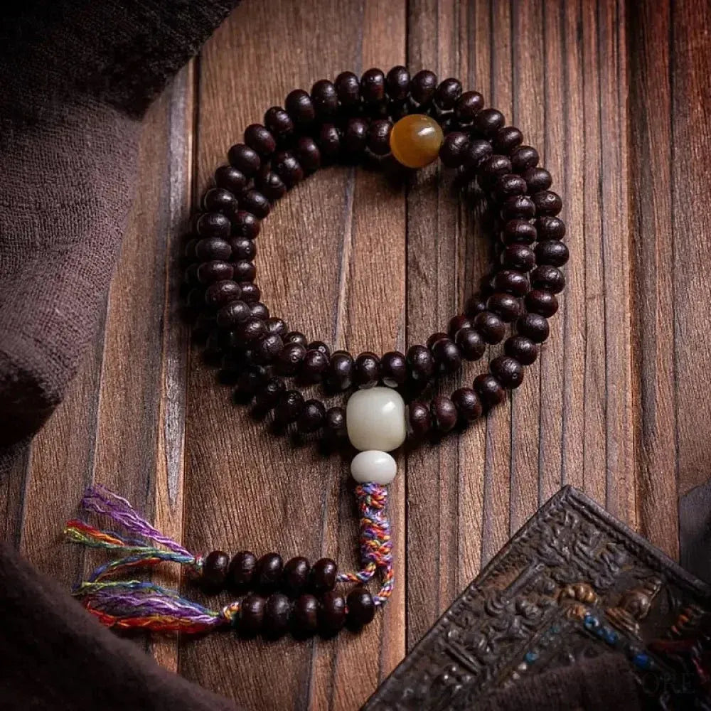A close-up of the BWOOOH 108 Mala Bracelet, showcasing polished red Bowl Bodhi seeds, each with a distinct 'eye,' intricately strung with a vibrant colored rope.
