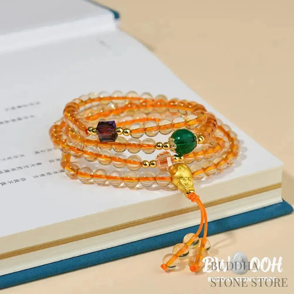 Main image of a BWOOOH 108 mala beads bracelet, crafted from polished natural citrine, with a prominent Liuli bead and alloy charm, resting on a serene, textured surface, ready for meditation and mindful reflection. - View 3