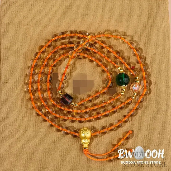 Main image of a BWOOOH 108 mala beads bracelet, crafted from polished natural citrine, with a prominent Liuli bead and alloy charm, resting on a serene, textured surface, ready for meditation and mindful reflection. - View 8