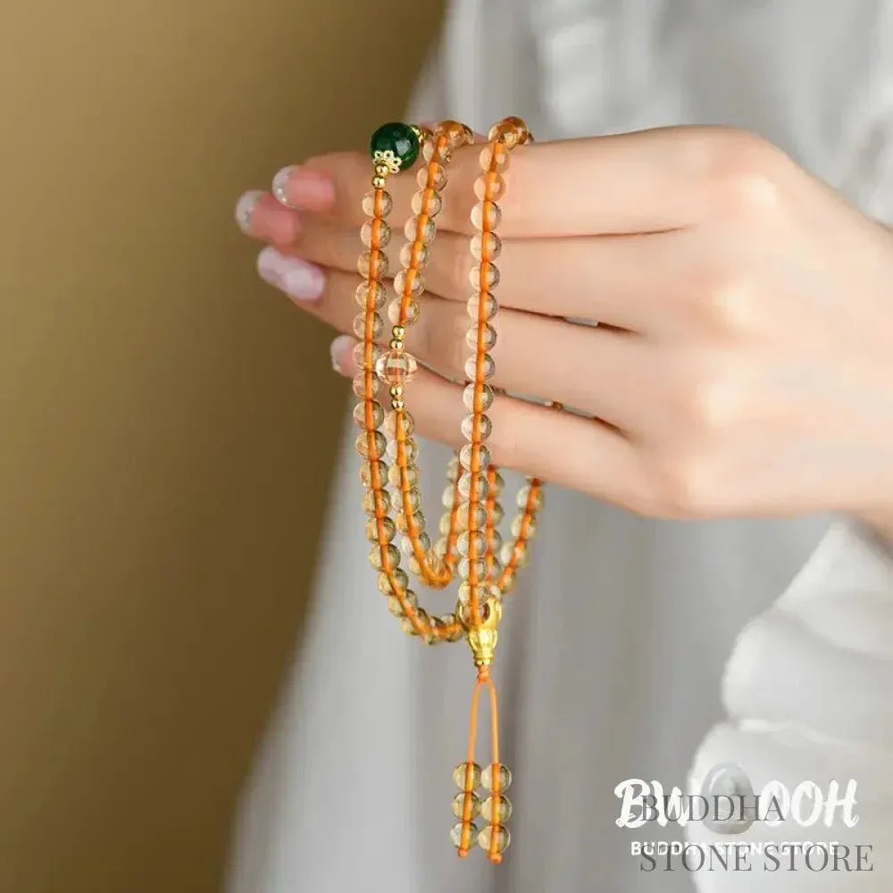 Main image of a BWOOOH 108 mala beads bracelet, crafted from polished natural citrine, with a prominent Liuli bead and alloy charm, resting on a serene, textured surface, ready for meditation and mindful reflection. - View 7