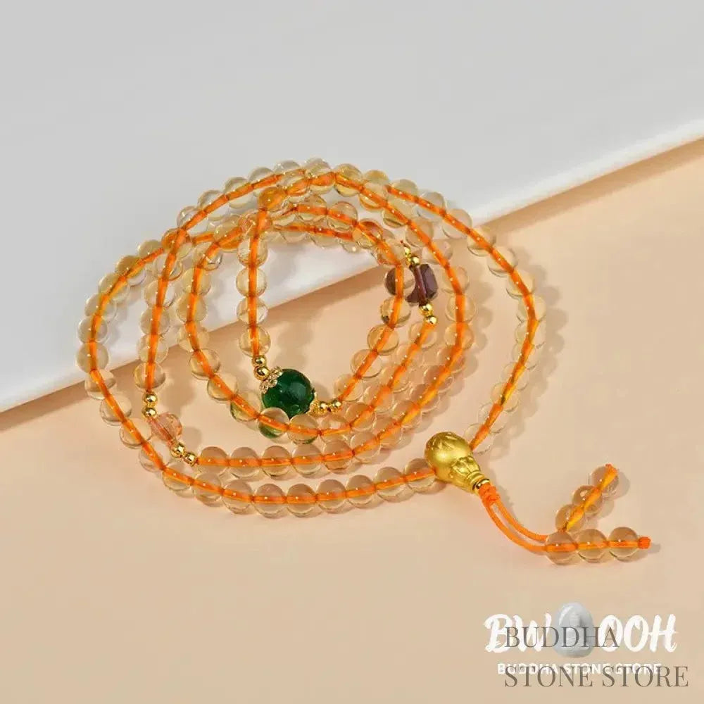 Main image of a BWOOOH 108 mala beads bracelet, crafted from polished natural citrine, with a prominent Liuli bead and alloy charm, resting on a serene, textured surface, ready for meditation and mindful reflection. - View 5