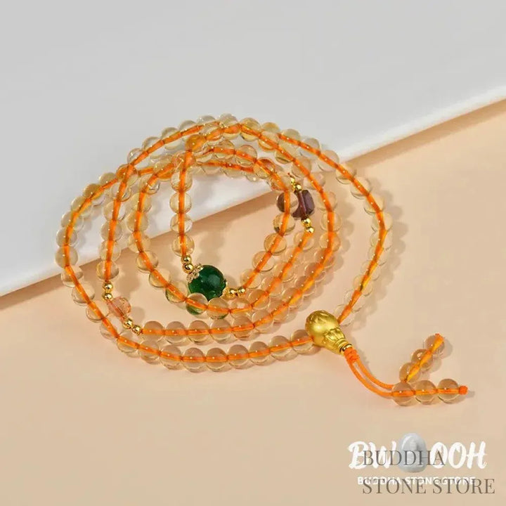 Main image of a BWOOOH 108 mala beads bracelet, crafted from polished natural citrine, with a prominent Liuli bead and alloy charm, resting on a serene, textured surface, ready for meditation and mindful reflection. - View 5