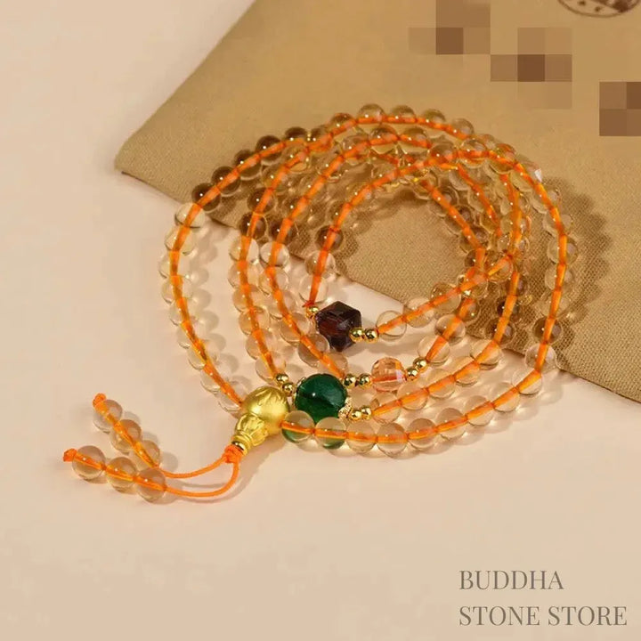 Main image of a BWOOOH 108 mala beads bracelet, crafted from polished natural citrine, with a prominent Liuli bead and alloy charm, resting on a serene, textured surface, ready for meditation and mindful reflection.