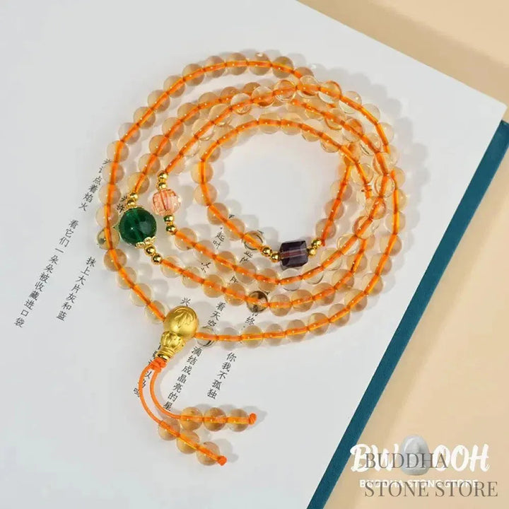 Main image of a BWOOOH 108 mala beads bracelet, crafted from polished natural citrine, with a prominent Liuli bead and alloy charm, resting on a serene, textured surface, ready for meditation and mindful reflection. - View 2