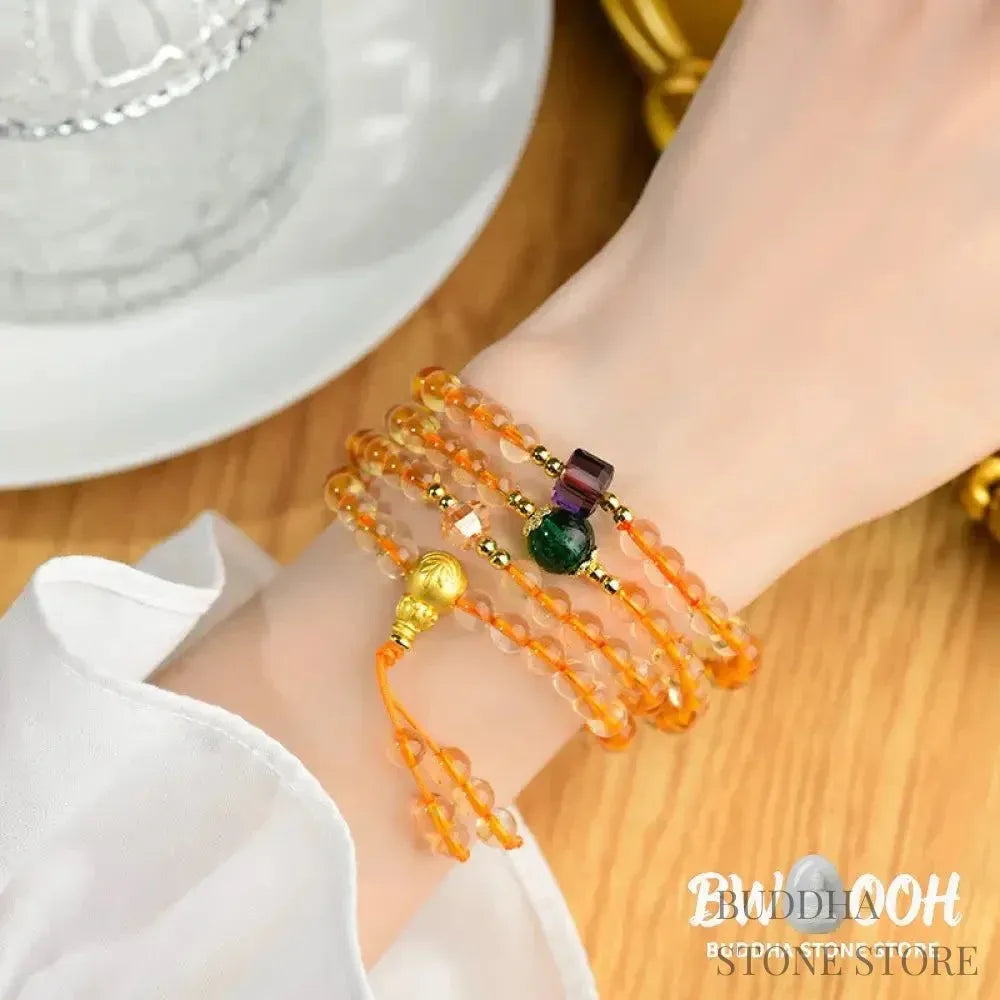 Main image of a BWOOOH 108 mala beads bracelet, crafted from polished natural citrine, with a prominent Liuli bead and alloy charm, resting on a serene, textured surface, ready for meditation and mindful reflection. - View 4