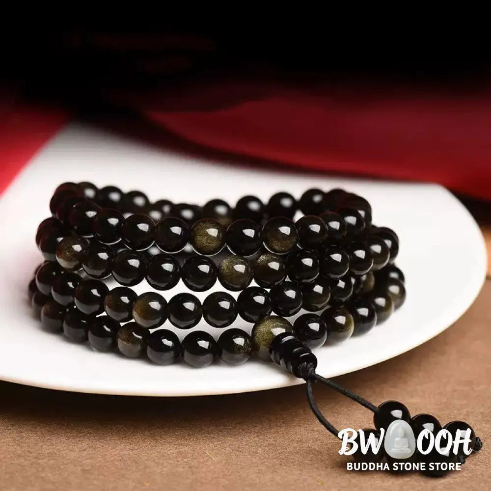 A close-up of the BWOOOH 108 Mala Beads Natural Gold Sheen Obsidian Wealth Bracelet, showcasing the distinctive golden sheen and polished dark beads, worn on a wrist. - View 2