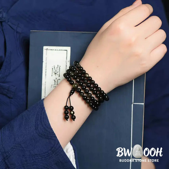 A close-up of the BWOOOH 108 Mala Beads Natural Gold Sheen Obsidian Wealth Bracelet, showcasing the distinctive golden sheen and polished dark beads, worn on a wrist. - View 5