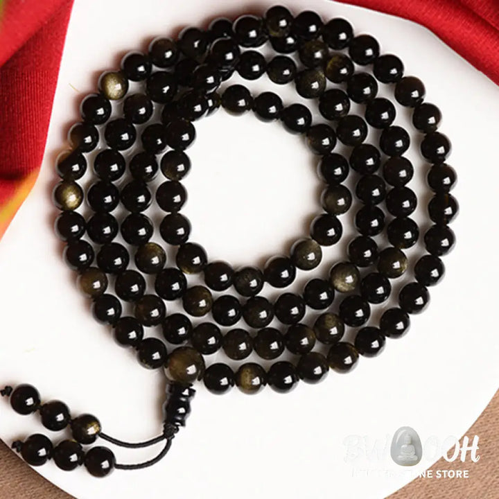 A close-up of the BWOOOH 108 Mala Beads Natural Gold Sheen Obsidian Wealth Bracelet, showcasing the distinctive golden sheen and polished dark beads, worn on a wrist. - View 12