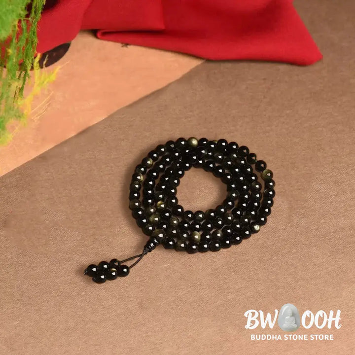 A close-up of the BWOOOH 108 Mala Beads Natural Gold Sheen Obsidian Wealth Bracelet, showcasing the distinctive golden sheen and polished dark beads, worn on a wrist. - View 9
