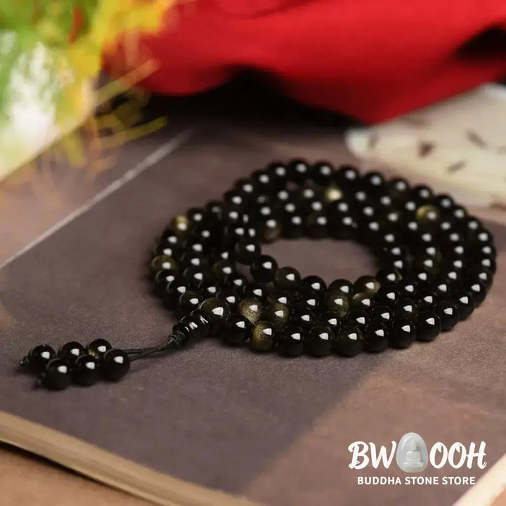 A close-up of the BWOOOH 108 Mala Beads Natural Gold Sheen Obsidian Wealth Bracelet, showcasing the distinctive golden sheen and polished dark beads, worn on a wrist. - View 3