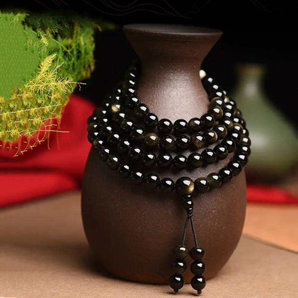 A close-up of the BWOOOH 108 Mala Beads Natural Gold Sheen Obsidian Wealth Bracelet, showcasing the distinctive golden sheen and polished dark beads, worn on a wrist.