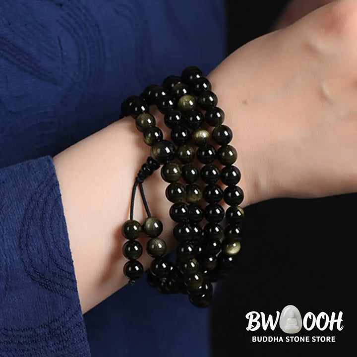 A close-up of the BWOOOH 108 Mala Beads Natural Gold Sheen Obsidian Wealth Bracelet, showcasing the distinctive golden sheen and polished dark beads, worn on a wrist. - View 11