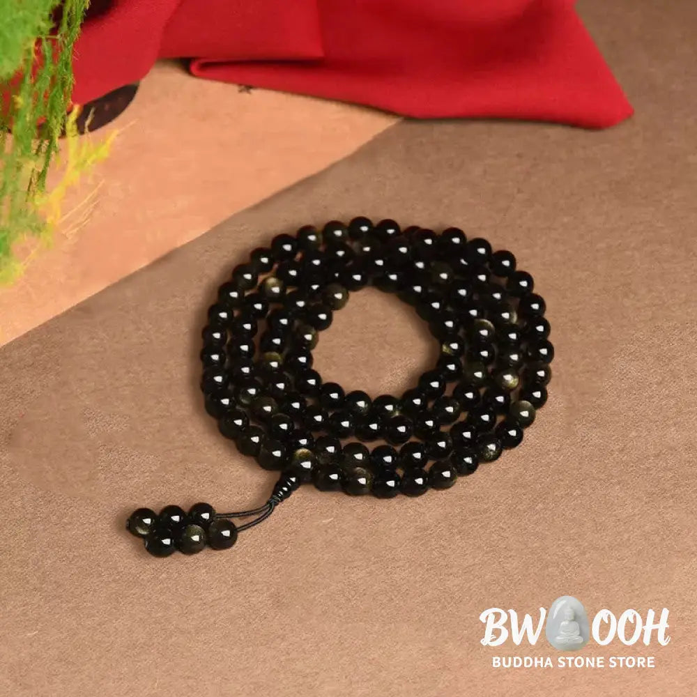 A close-up of the BWOOOH 108 Mala Beads Natural Gold Sheen Obsidian Wealth Bracelet, showcasing the distinctive golden sheen and polished dark beads, worn on a wrist. - View 10