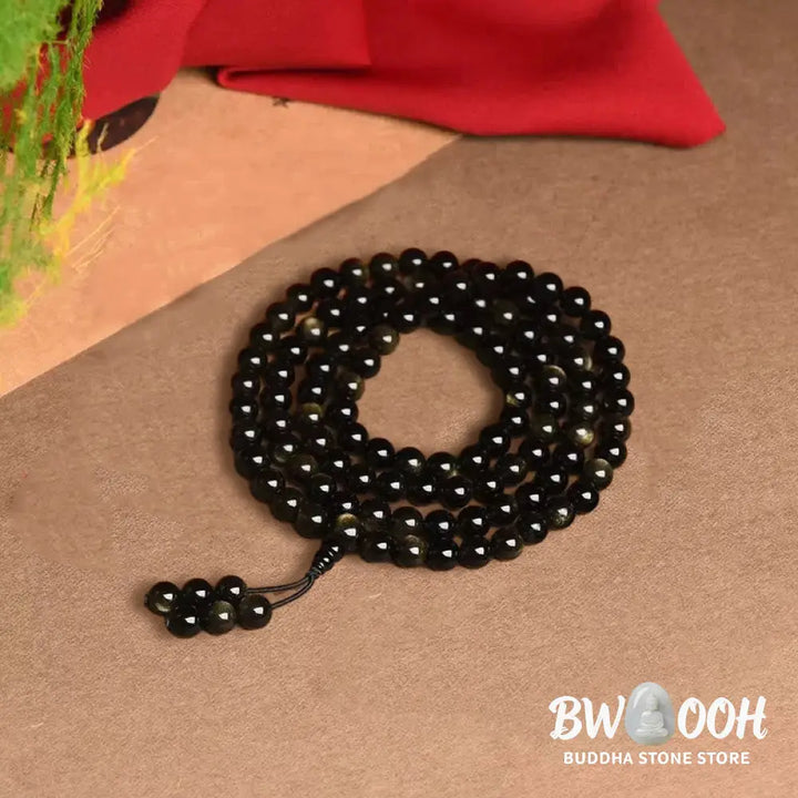 A close-up of the BWOOOH 108 Mala Beads Natural Gold Sheen Obsidian Wealth Bracelet, showcasing the distinctive golden sheen and polished dark beads, worn on a wrist. - View 10