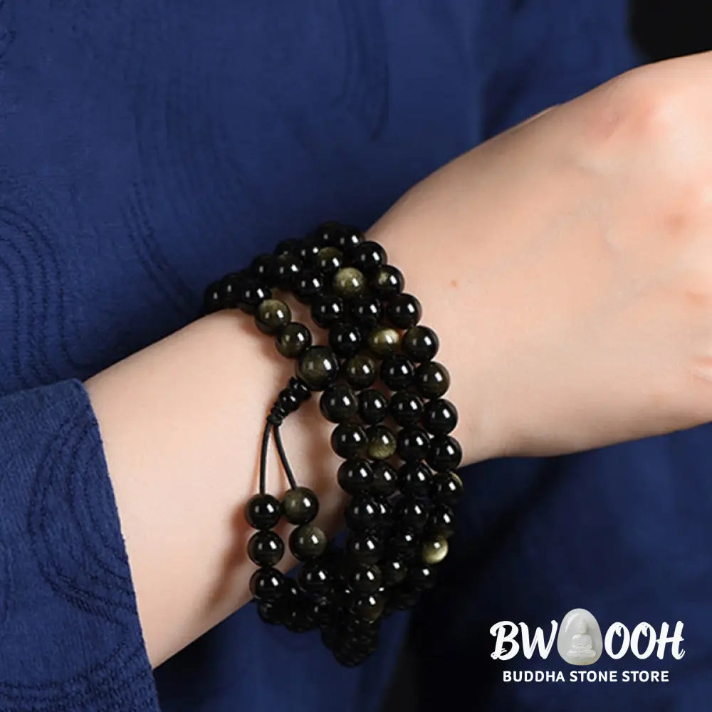 A close-up of the BWOOOH 108 Mala Beads Natural Gold Sheen Obsidian Wealth Bracelet, showcasing the distinctive golden sheen and polished dark beads, worn on a wrist. - View 7