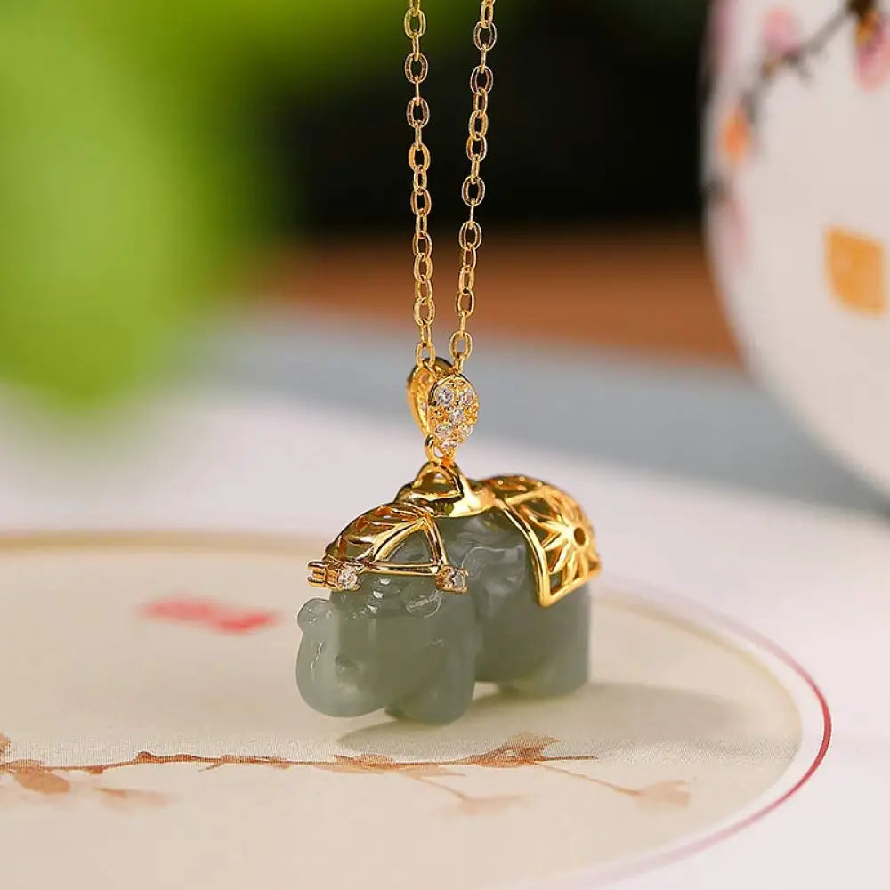 A close-up of the BWOOOH 925 Sterling Silver gold-plated elephant pendant, intricately carved and holding a vibrant jade stone, against a minimalist backdrop, highlighting its 45cm chain.