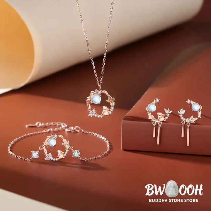 A complete BWOOOH 925 Sterling Silver Year of the Rabbit Moonstone Moon Flower Pattern Necklace, Pendant, Bracelet, and Earrings set on a serene, reflective surface. Each piece features natural moonstone with its ethereal blue adularescence, set in intricate silver moon flower motifs. The pendant prominently displays the rabbit emblem, symbolizing peace, elegance, and good fortune, evoking spiritual balance. - View 3