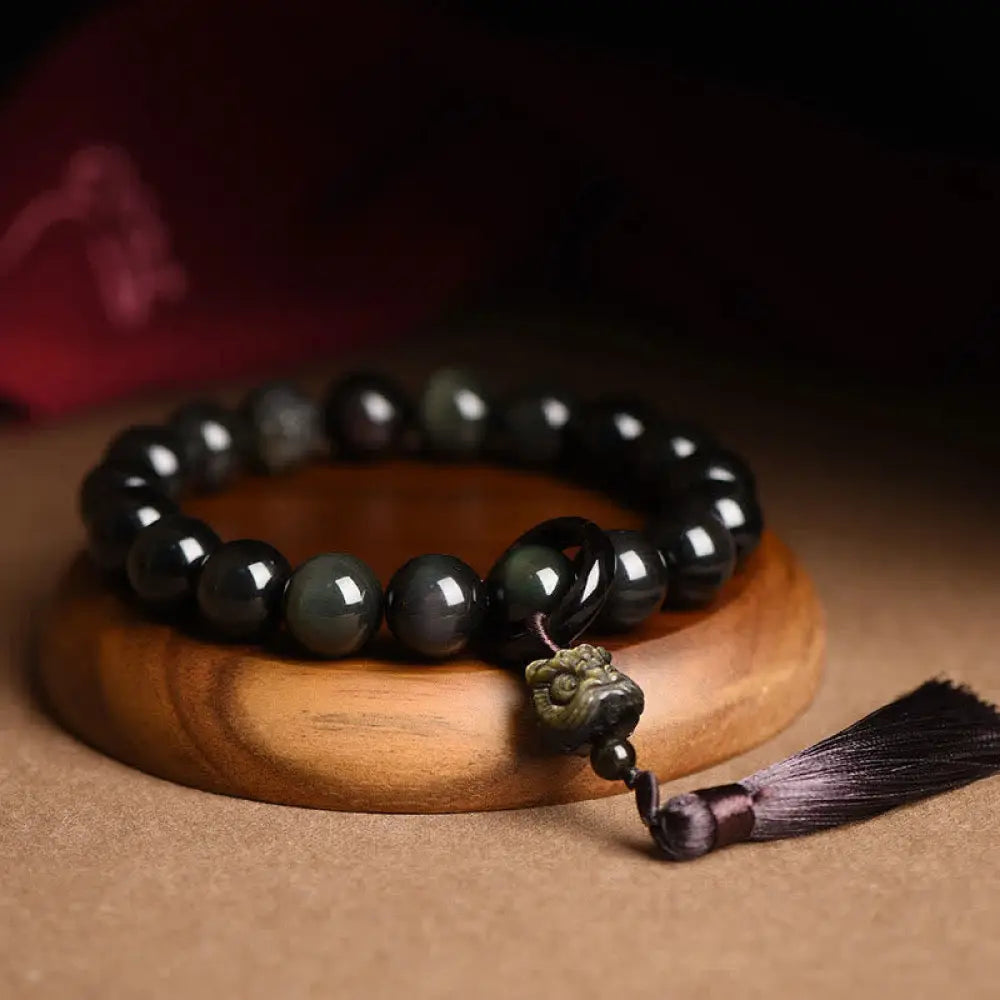 A BWOOOH Natural Black Obsidian Lion Wrist Mala with protection tassels, shown as a pocket mala and car decoration, embodying courage, wisdom, and spiritual enlightenment for energetic protection and positive Feng Shui.