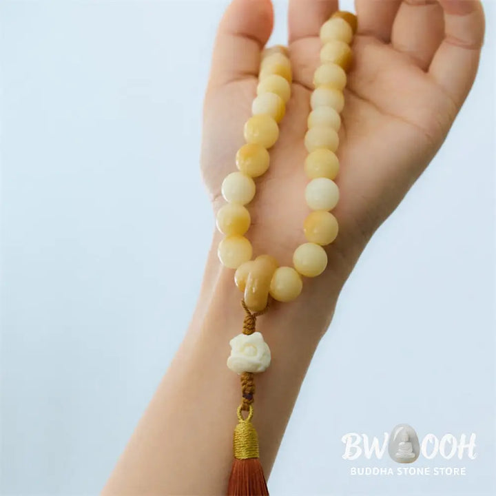 A close-up of the BWOOOH Natural Bodhi Seed Ivory Fruit Dancing Lion Charm Harmony Tassel Wrist Mala, featuring 12mm dark-speckled Bodhi Seed beads, smooth Ivory Fruit accents, and a detailed golden Dancing Lion charm with a vibrant harmony tassel, set against a muted, calming background. - View 4