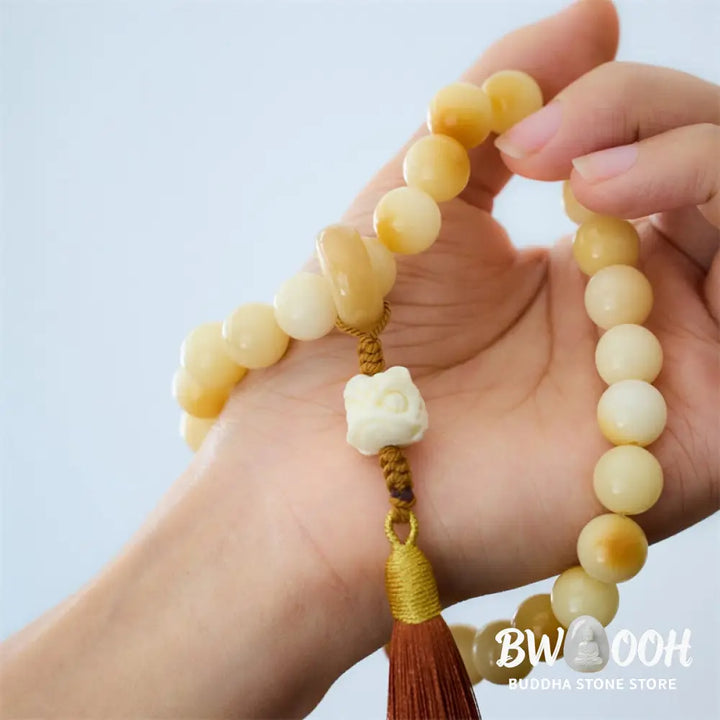 A close-up of the BWOOOH Natural Bodhi Seed Ivory Fruit Dancing Lion Charm Harmony Tassel Wrist Mala, featuring 12mm dark-speckled Bodhi Seed beads, smooth Ivory Fruit accents, and a detailed golden Dancing Lion charm with a vibrant harmony tassel, set against a muted, calming background. - View 2