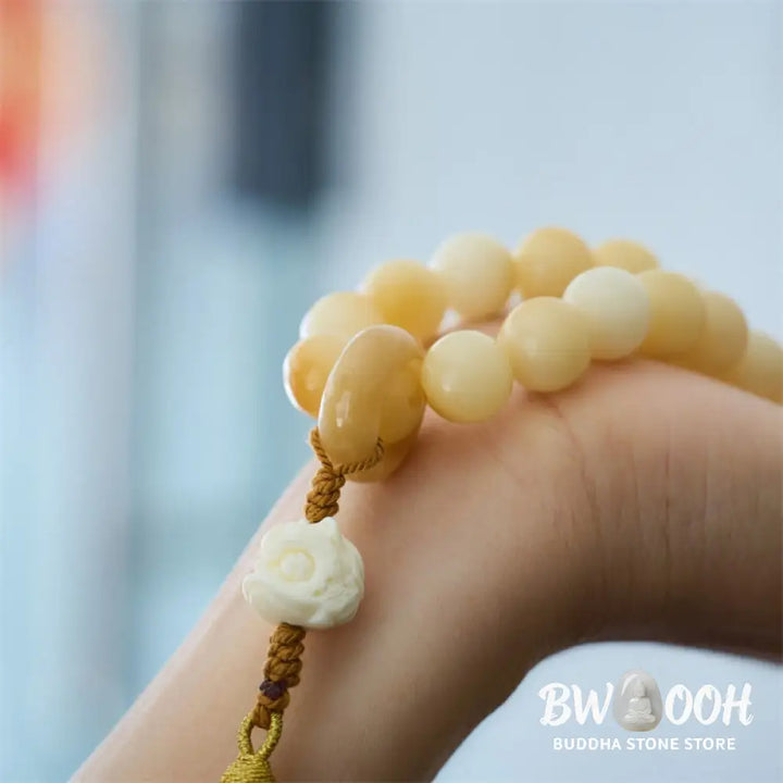 A close-up of the BWOOOH Natural Bodhi Seed Ivory Fruit Dancing Lion Charm Harmony Tassel Wrist Mala, featuring 12mm dark-speckled Bodhi Seed beads, smooth Ivory Fruit accents, and a detailed golden Dancing Lion charm with a vibrant harmony tassel, set against a muted, calming background. - View 3