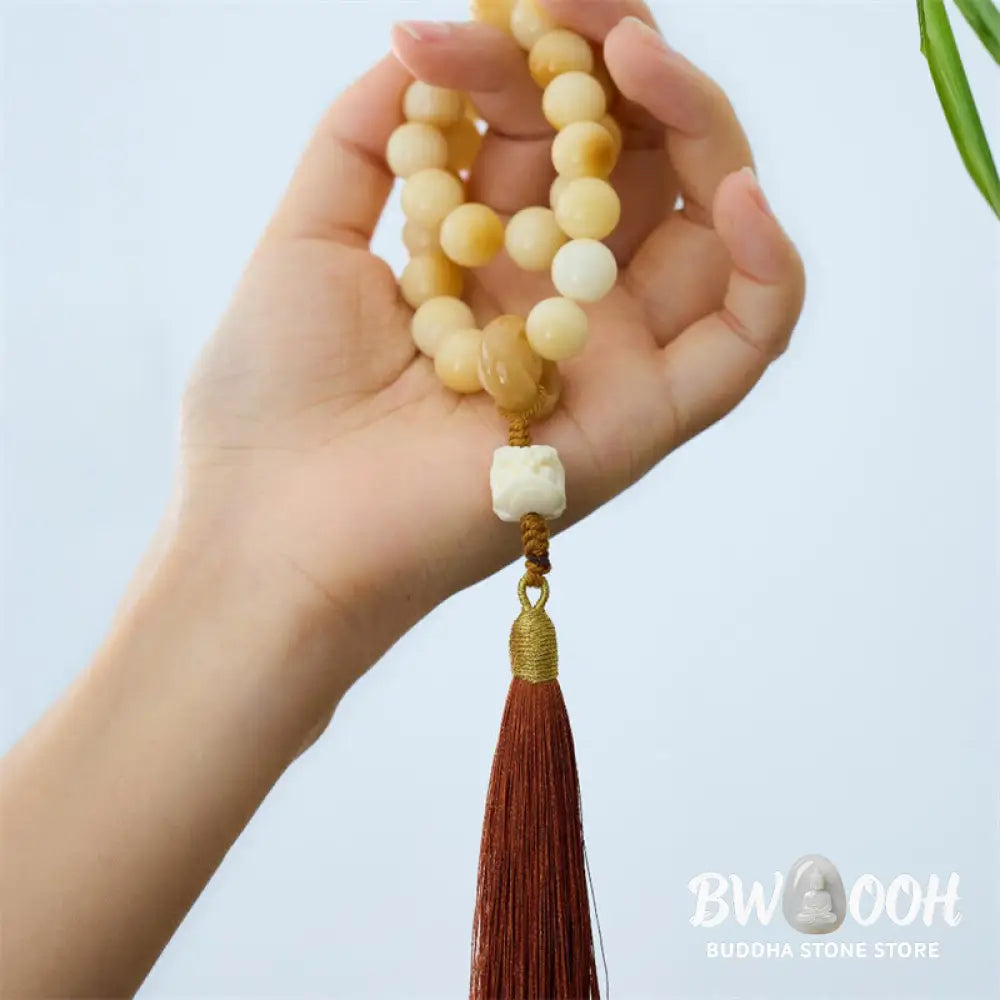 A close-up of the BWOOOH Natural Bodhi Seed Ivory Fruit Dancing Lion Charm Harmony Tassel Wrist Mala, featuring 12mm dark-speckled Bodhi Seed beads, smooth Ivory Fruit accents, and a detailed golden Dancing Lion charm with a vibrant harmony tassel, set against a muted, calming background. - View 5